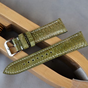May include: Two green leather watch straps with white stitching. The straps are laid out on a wooden surface.