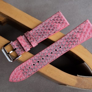 May include: Two pink leather watch straps with a textured pattern, displayed on a wooden watch strap holder.