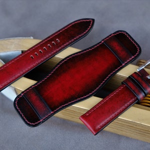 May include: Three red leather watch straps with black stitching. The straps are laid out on a wooden surface. The straps have a distressed look and are made of high-quality leather.