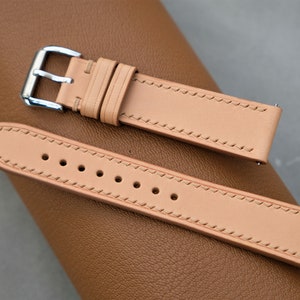May include: Two light brown leather watch straps with stitching detail. The strap on top has a silver buckle. The strap on the bottom has six holes for adjusting the fit.