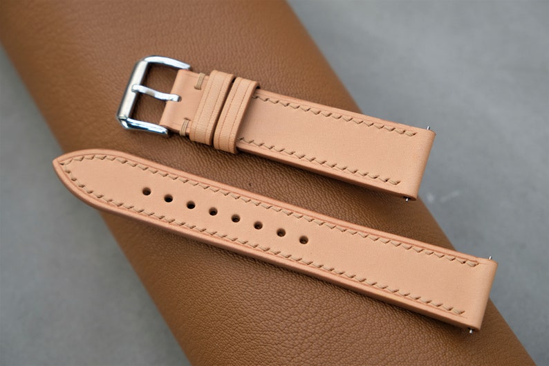 May include: Two light brown leather watch straps with stitching detail. The strap on top has a silver buckle. The strap on the bottom has six holes for adjusting the fit.