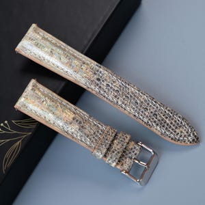 May include: Two watch straps with a silver and gold iridescent pattern. The straps are made of leather and have a buckle closure.