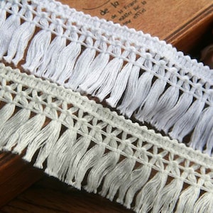 May include: Two white cotton fringe trims with a delicate crochet pattern. The fringe is approximately 2.5 cm long.