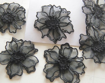May include: Seven black lace flower appliques with a delicate, intricate design. The appliques are made of a sheer, lightweight fabric and have a slightly ruffled edge.