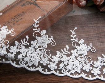 May include: White floral lace trim with a scalloped edge. The delicate embroidery features detailed flowers and leaves. This lace is ideal for adding a touch of elegance to various craft projects.