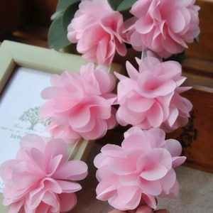 May include: A string of pink fabric flowers, each flower is made of multiple layers of soft fabric, creating a fluffy and delicate look. The flowers are arranged in a row, creating a beautiful and feminine design.