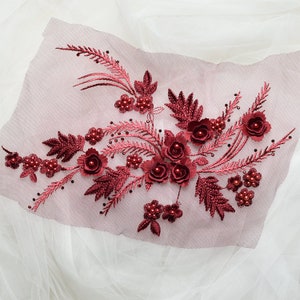 Peut inclure: Applique florale bordeaux avec des accents de perles. L'applique présente un groupe de fleurs et de feuilles 3D, parfait pour ajouter une touche d'élégance aux vêtements ou aux objets artisanaux.