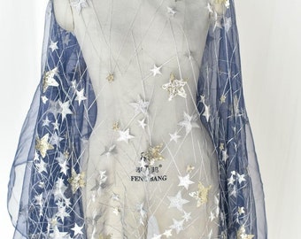 May include: Navy blue tulle fabric with gold and silver glitter stars embroidered on it. The fabric is draped over a dress form. The text "FENG BANG" is visible on the fabric.