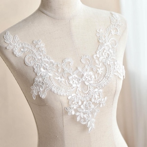 Peut inclure: Applique en dentelle blanche avec un motif floral. La dentelle est délicate et complexe, avec un bord festonné. Cette applique serait parfaite pour ajouter une touche d'élégance à une robe de mariée, une robe de mariée ou une autre tenue de cérémonie.