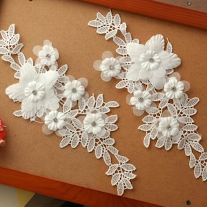 May include: Two white lace appliques with floral designs and rhinestone accents. The appliques are perfect for adding a touch of elegance to any project.