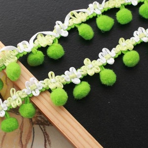 Peut inclure: Garniture verte et blanche avec des pompons. La garniture est faite d'un tissu doux et tissé et a un aspect délicat et féminin.