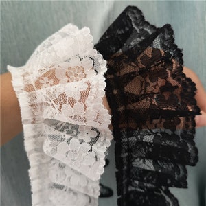 Könnte beinhalten: Zwei Stücke Spitzenborte, eine weiße und eine schwarze, mit einem gekräuselten Rand und einem Blumenmuster.