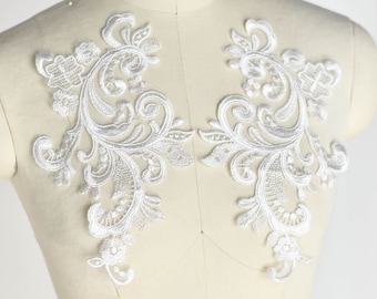 Könnte beinhalten: Zwei weiße Spitzenapplikationen mit floralem Design. Die Applikationen sind perfekt, um jedem Kleidungsstück einen Hauch von Eleganz zu verleihen.