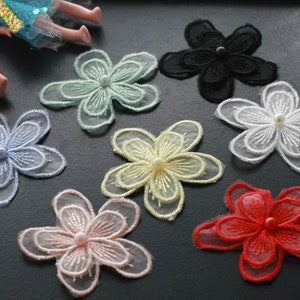 May include: Assortment of seven delicate flower-shaped fabric appliques in various colors, including light blue, light green, white, yellow, pink, red, and black. Each applique features a pearl-like embellishment in the center.