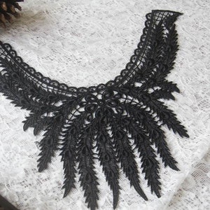 Puede incluir: Adorno de encaje negro con borde festoneado y un delicado diseño floral. El encaje tiene un efecto en cascada con hebras largas y delgadas.