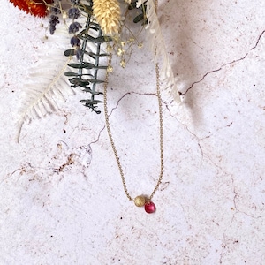 May include: A delicate gold chain necklace with a small gold bead and a pink gemstone pendant.