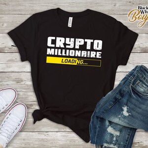 Puede incluir: Camiseta negra con texto blanco que dice "CRYPTO MILLIONAIRE LOADING..." con una barra de progreso amarilla.