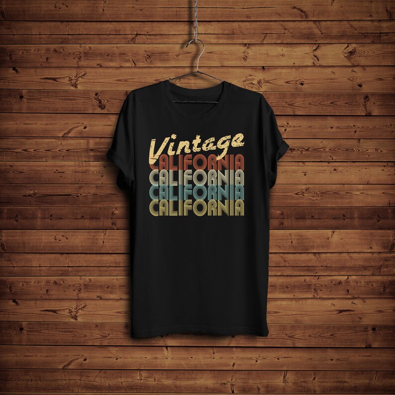 Op de afbeelding: Zwart T-shirt met een vintage-stijl grafische afbeelding met de tekst "Vintage California" in een gelaagd, retro lettertype met de kleuren rood, oranje, geel en blauw.
