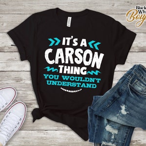 Puede incluir: Camiseta negra con texto blanco que dice "It's a Carson thing you wouldn't understand". El texto está rodeado de líneas onduladas azules y flechas.