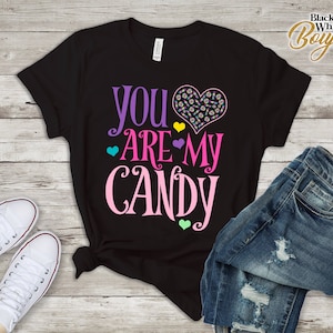 Puede incluir: Camiseta negra con el texto "You are my candy" en letras rosa, morado y amarillo. Un corazón con diseños de caramelos está por encima del texto.
