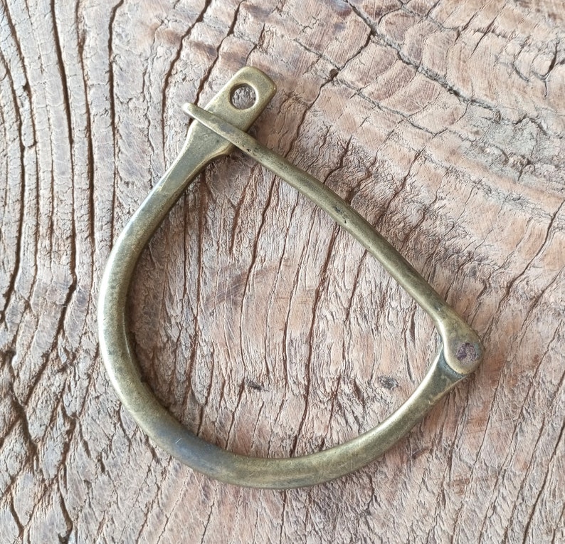 Puede incluir: Un anillo de lat&oacute;n en forma de D con un borde redondeado. El anillo es liso y tiene un acabado ligeramente desgastado.