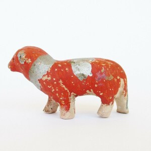 May include: A small, red and silver painted ceramic animal figurine. The figurine is of a sheep with a standing pose.