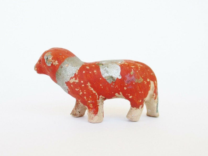 May include: A small, red and silver painted ceramic animal figurine. The figurine is of a sheep with a standing pose.