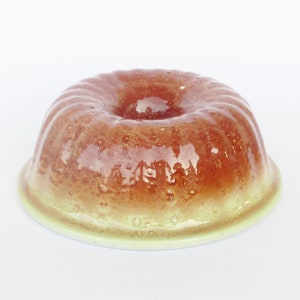 May include: A glazed ceramic bundt cake pan with a light green base and a brown glaze. The pan has a ring in the center and is designed to bake a bundt cake.
