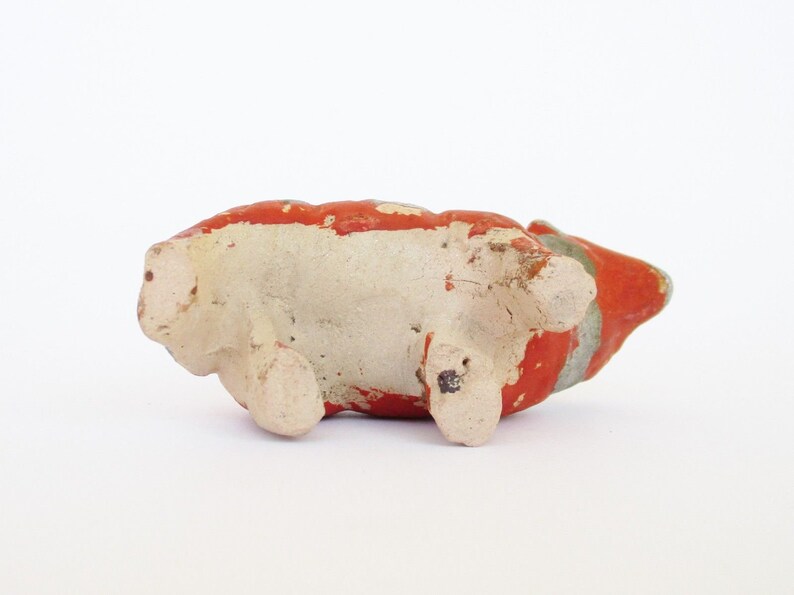 May include: A small ceramic pig figurine with red, white, and gray paint. The pig is lying on its side with its legs visible.