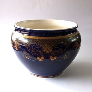 Può includere: Un vaso in ceramica blu cobalto con disegni floreali dorati. Il vaso ha una forma arrotondata e un bordo largo.