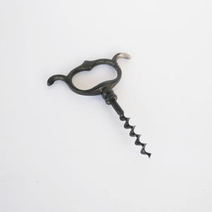 May include: A vintage black corkscrew with a decorative handle and a spiral worm. The handle has a heart-shaped design. The corkscrew is made of metal and has a silver-coloured tip.