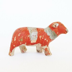 May include: A small, red and white ceramic sheep figurine. The sheep is standing on all four legs and has a slightly tilted head. The figurine is painted with a red base and white accents.