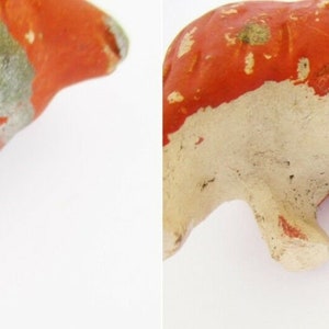 May include: A small, hand-painted, ceramic cow figurine with a white body and orange and gray markings. The cow is standing on all four legs.