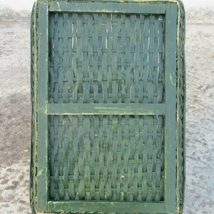 Op de afbeelding: Een groene geweven mand met een houten frame. De mand is gemaakt van natuurlijke materialen en heeft een rustieke uitstraling.