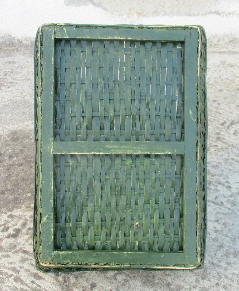 Op de afbeelding: Een groene geweven mand met een houten frame. De mand is gemaakt van natuurlijke materialen en heeft een rustieke uitstraling.