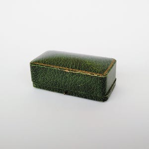 May include: A small, green, rectangular box with a textured surface. The box has a gold trim around the edges.
