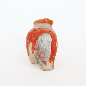 May include: Red and white ceramic animal figurine with holes in the back. The figurine is standing on a white surface.