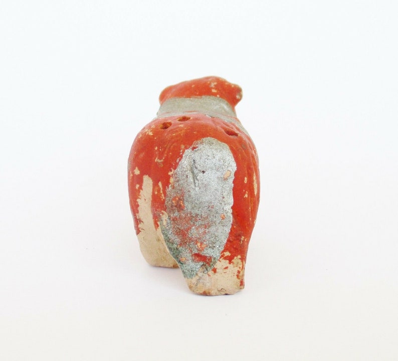May include: Red and white ceramic animal figurine with holes in the back. The figurine is standing on a white surface.