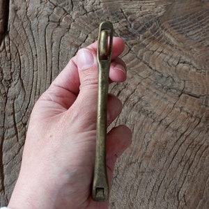 Puede incluir: Un tirador de caj&oacute;n de lat&oacute;n con un dise&ntilde;o simple y recto. El tirador tiene una parte superior redondeada y una base rectangular.