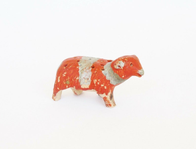 May include: A small, red and white ceramic sheep figurine with a hole in its back. The sheep is standing on a white surface.