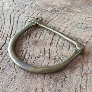 Puede incluir: Un brazalete de lat&oacute;n con un cierre de bisagra. El brazalete tiene un dise&ntilde;o simple y curvo.