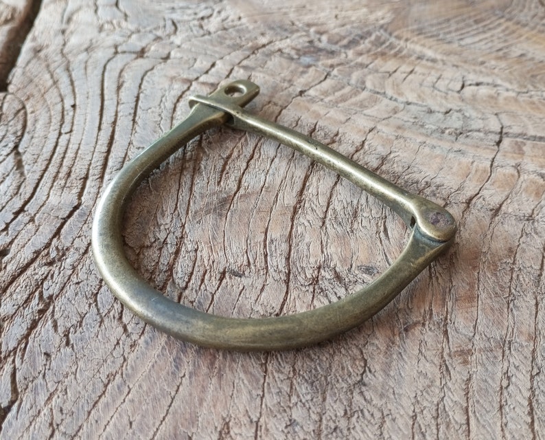 Puede incluir: Un brazalete de lat&oacute;n con un cierre de bisagra. El brazalete tiene un dise&ntilde;o simple y curvo.