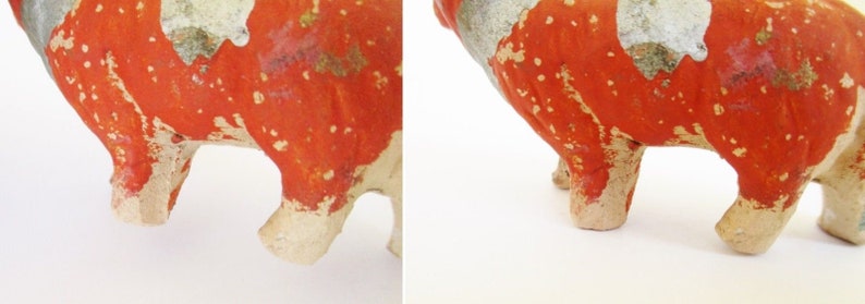 May include: A ceramic pig figurine with red and white paint. The pig is standing on all four legs and has a chipped paint finish.