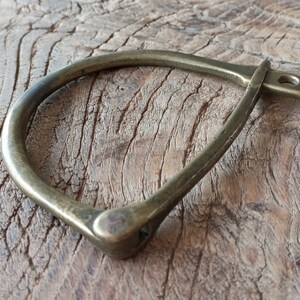 Puede incluir: Un brazalete de lat&oacute;n en forma de herradura con un dise&ntilde;o simple y minimalista. El brazalete es liso y pulido, con un acabado ligeramente desgastado.