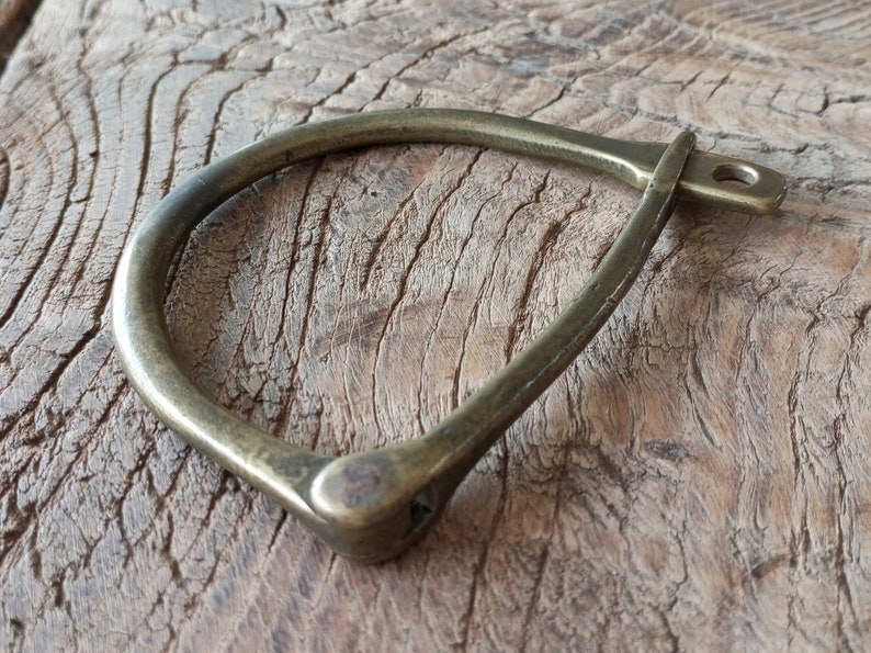 Puede incluir: Un brazalete de lat&oacute;n en forma de herradura con un dise&ntilde;o simple y minimalista. El brazalete es liso y pulido, con un acabado ligeramente desgastado.
