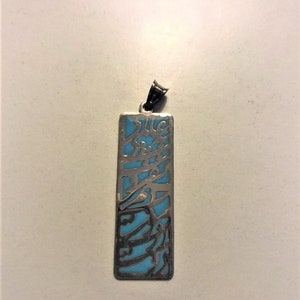 Peut inclure: Un pendentif en argent avec une incrustation d'émail bleu. Le pendentif est rectangulaire et présente des motifs découpés complexes.