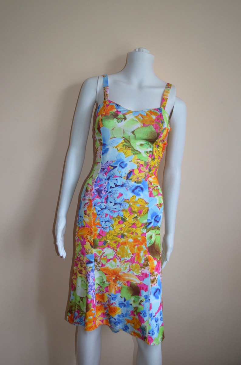 Puede incluir: Un vestido sin mangas con estampado floral en tonos azules, amarillos, rosas y verdes. El vestido tiene un corpi&ntilde;o ajustado y una falda acampanada.