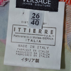 Puede incluir: Una etiqueta blanca con texto negro que dice "VERSACE JEANS COUTURE" y una etiqueta blanca m&aacute;s peque&ntilde;a con texto negro que dice "26/40" y "ITTIERRE S.P.A. Pettoranello ci Molise-ISERNIA ITALIA" y "MADE IN ITALY FABRIQUE EN ITALIE PRODUCIDO NA ITALIA FABRICADO EN ITALIA イタリア製".