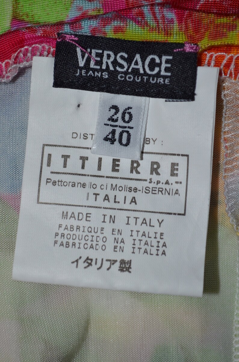 Puede incluir: Una etiqueta blanca con texto negro que dice "VERSACE JEANS COUTURE" y una etiqueta blanca m&aacute;s peque&ntilde;a con texto negro que dice "26/40" y "ITTIERRE S.P.A. Pettoranello ci Molise-ISERNIA ITALIA" y "MADE IN ITALY FABRIQUE EN ITALIE PRODUCIDO NA ITALIA FABRICADO EN ITALIA イタリア製".