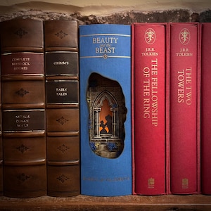 May include: A collection of hardcover books with titles including "Complete Sherlock Holmes", "Grimm's Fairy Tales", and "Beauty and the Beast". The "Beauty and the Beast" book has a cutout revealing a silhouette scene. The books are in various colors, including brown, blue, and red.